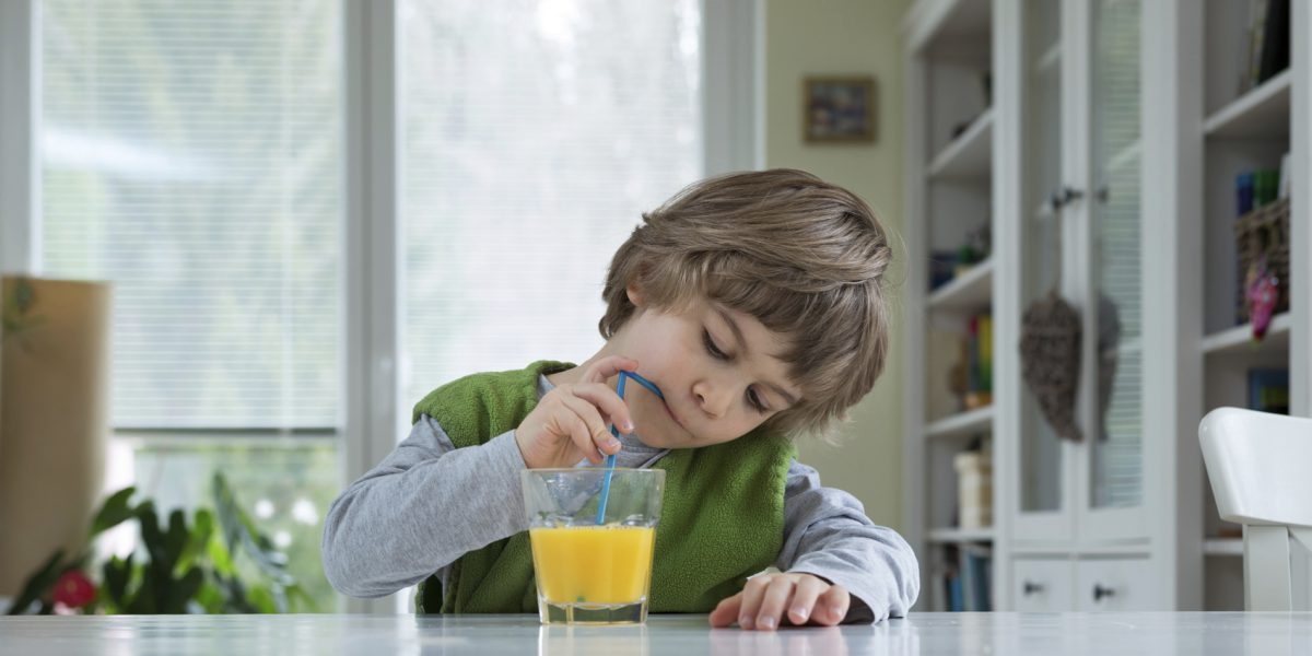 Cute little boy sitting at the table drinking orange juice for breakfast. Healthy lifestyle, nutrition and healthy eating